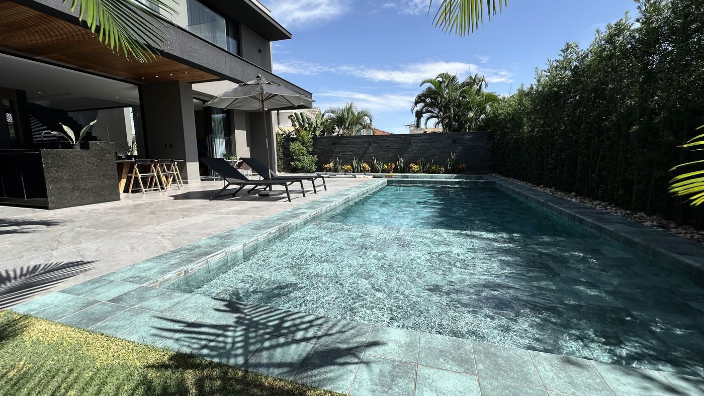 A piscina, com o deck de pedra e a casa ao fundo
